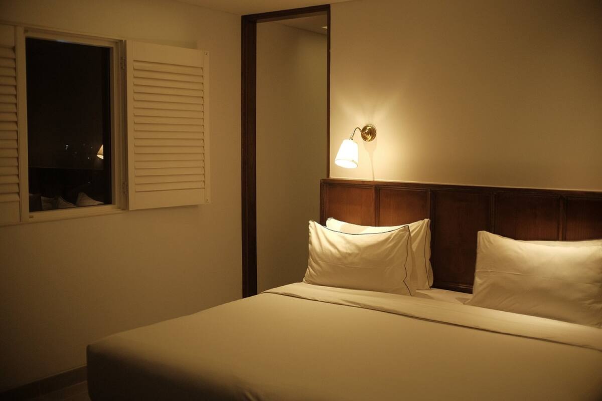Une chambre d’hôtel avec un lit, une table de chevet, un miroir et une fenêtre avec des stores.