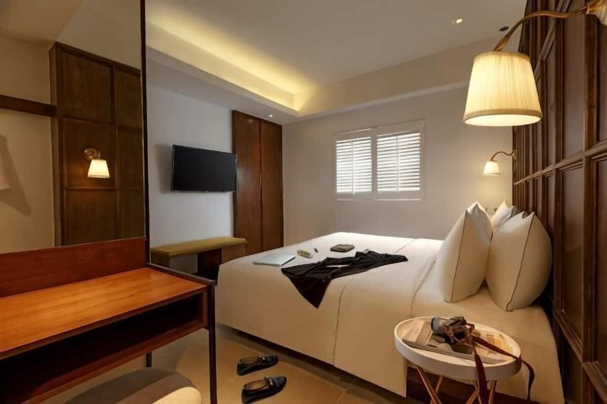 Une chambre d’hôtel avec un lit, un bureau, une chaise, une télévision et une fenêtre avec des stores.