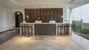 Un área de recepción moderna con un mostrador, dos taburetes de bar, una alfombra estampada y un amplio ventanal con vistas a la vegetación.