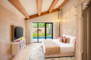 A bedroom with a large bed, a TV, a decorative cabinet, and a view of greenery outside. - Taj Aravali Resort & Spa (Udaipur)