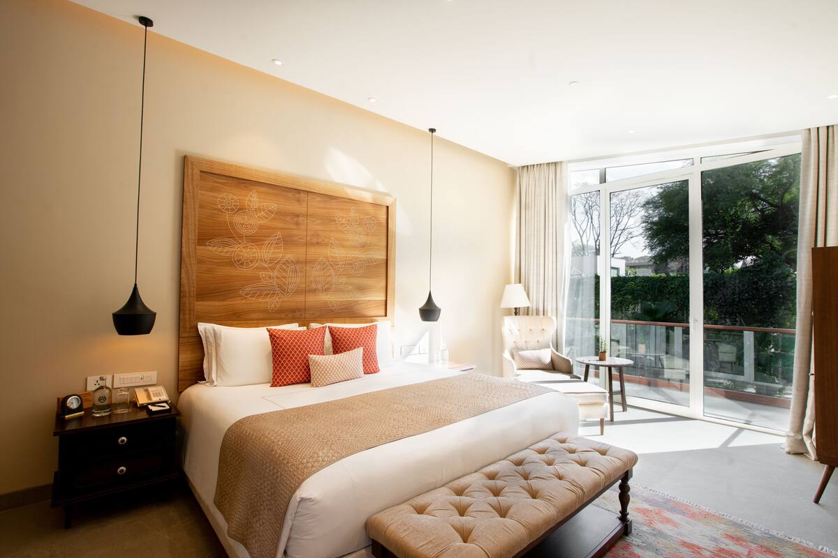 A modern hotel room with a large bed, a bench, a desk, and a balcony with a view.