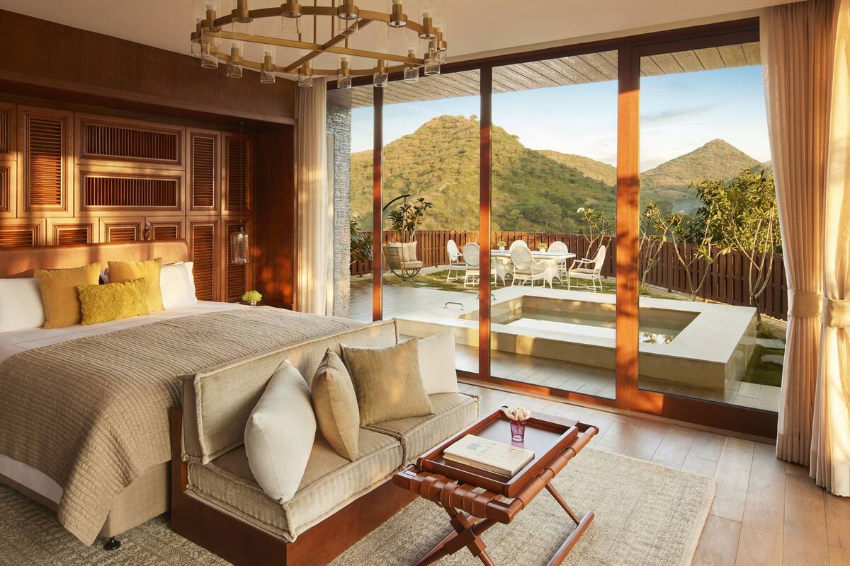 A spacious bedroom with a large bed, a sofa, and a view of a mountainous landscape through large windows.