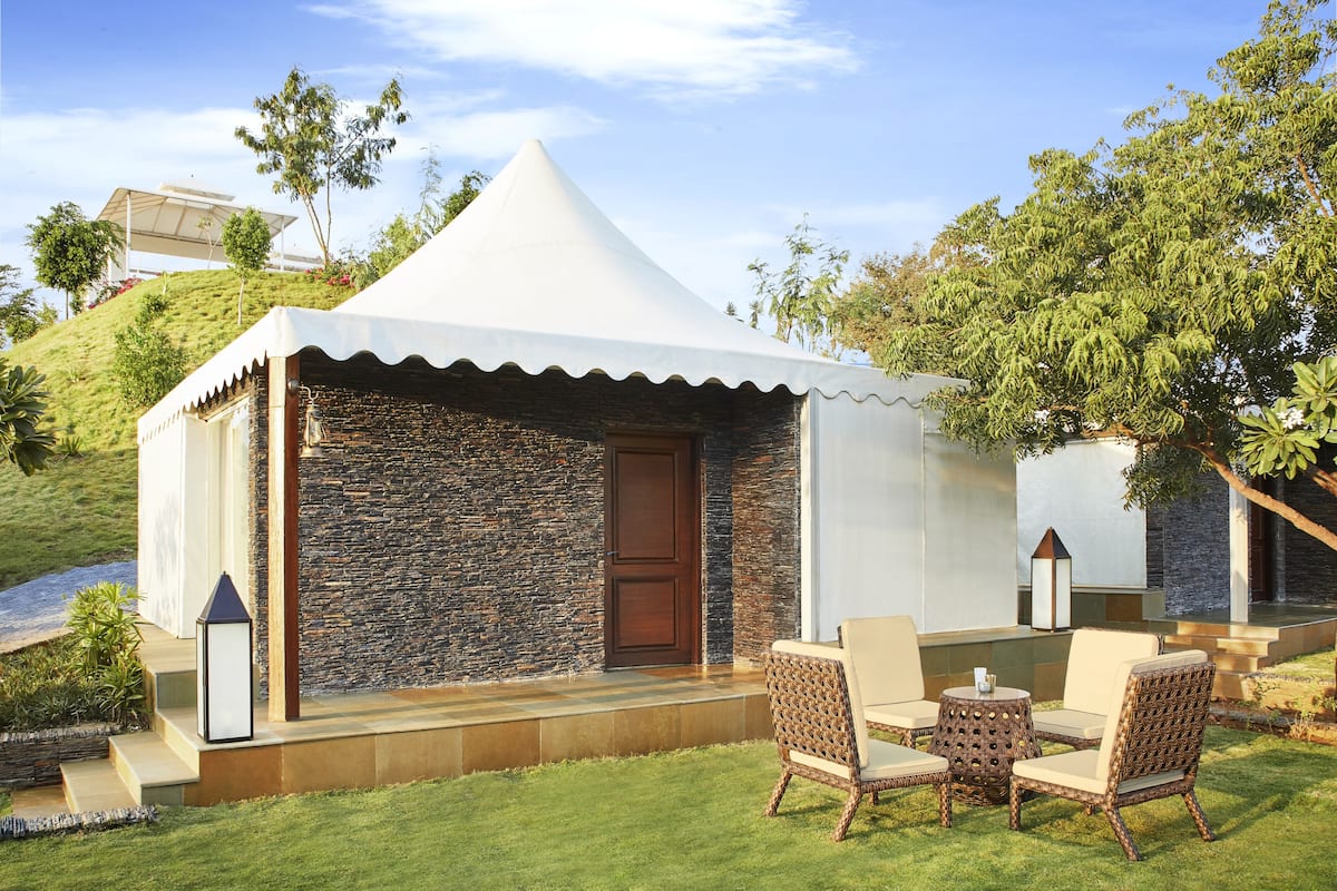 A tented outdoor area with stone walls, a wooden door, and wicker furniture.