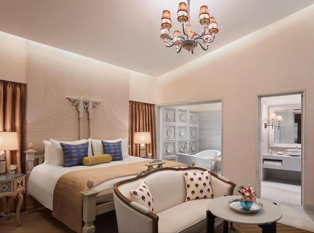 Hotelkamer met een bed, een bank, een ronde tafel, een kroonluchter, een badkamer met een bad en een grote spiegel.