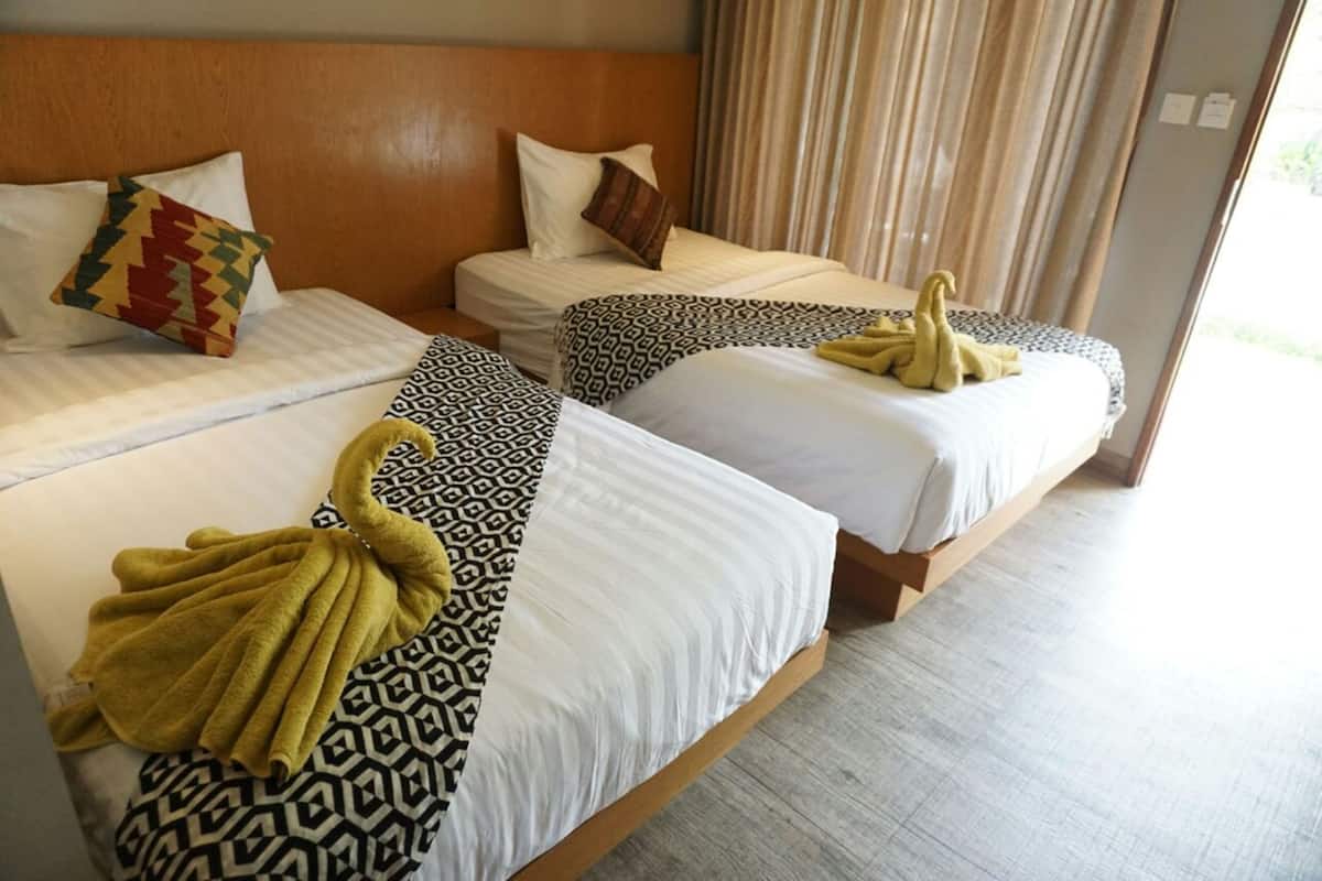 Hotellihuone, jossa on kolme sänkyä, ja jokaisessa sängyssä on kuviollinen vuodevaatteisto ja pyyhkeet.