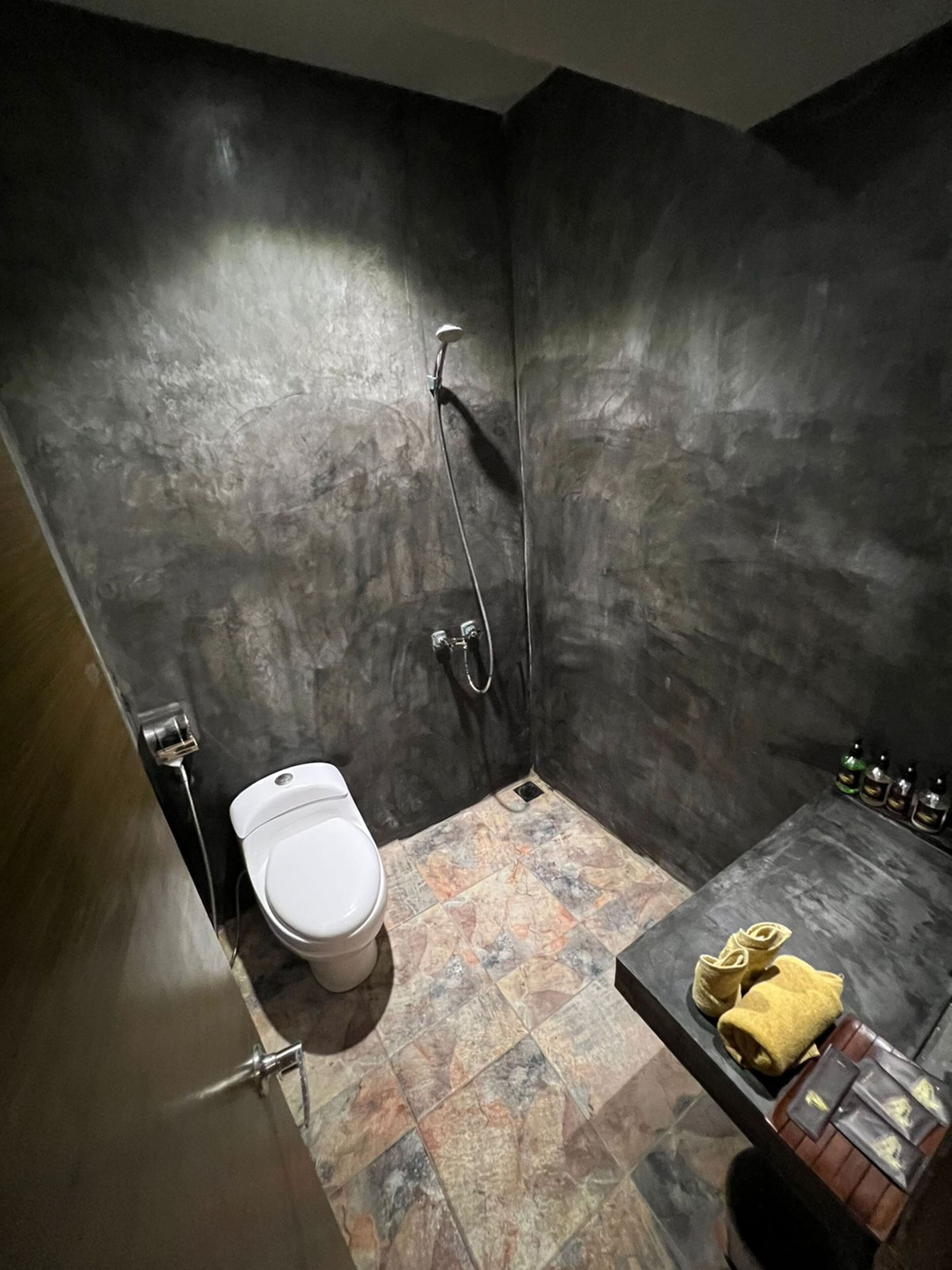 A small, dark-themed bathroom with a toilet, shower, and a sink area with toiletries.