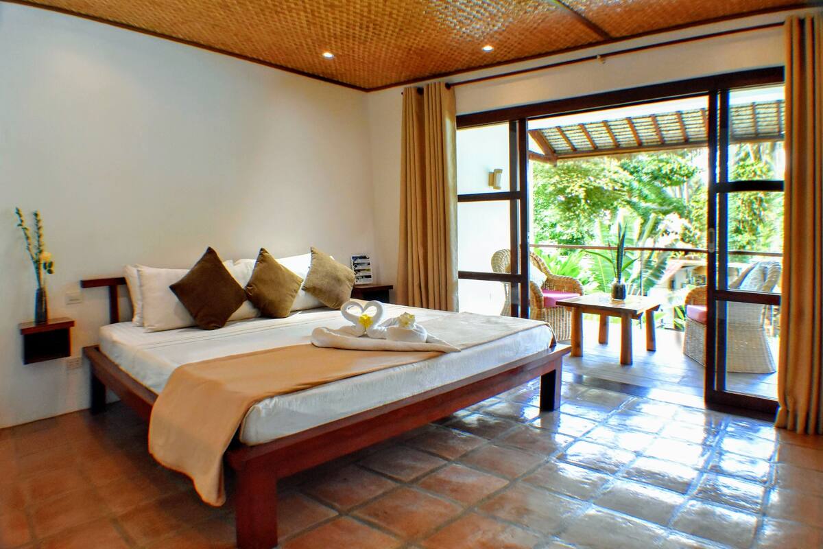 A hotel room with a large bed, a wooden headboard, a nightstand, and a view of the outdoors through a glass door.