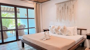A hotel room with a large bed, a macrame wall hanging, and a view of an outdoor area with wicker furniture. - El Nido Moringa Resort (El Nido)