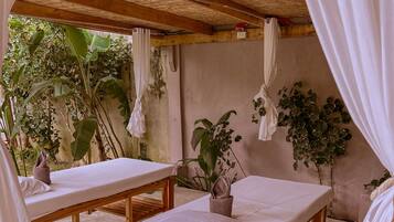 Relax in a serene spa area with two massage tables under a shaded roof, surrounded by lush greenery.