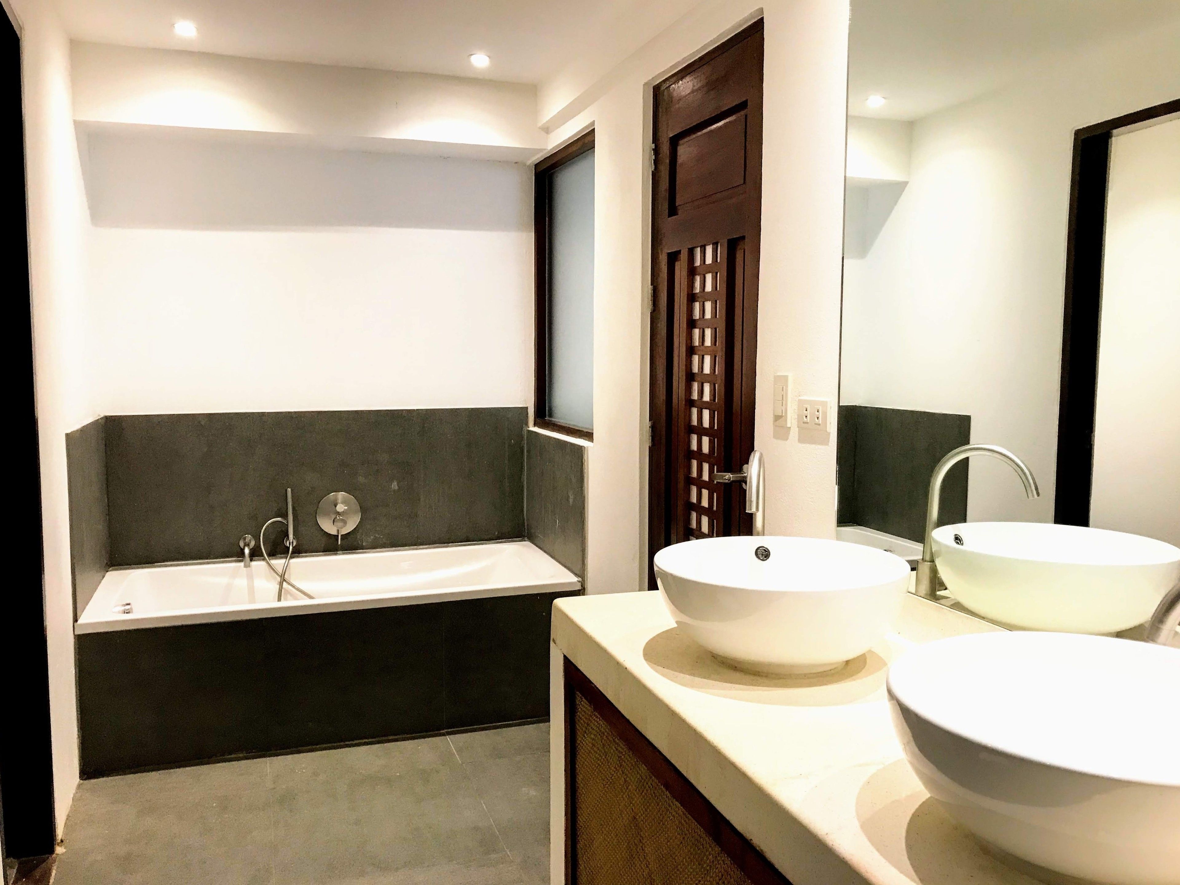 A modern bathroom with a bathtub, two sinks, and a large mirror.