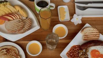 Una mesa de desayuno con diversos alimentos, como panqueques, tostadas, frijoles, huevos y una cafetera.