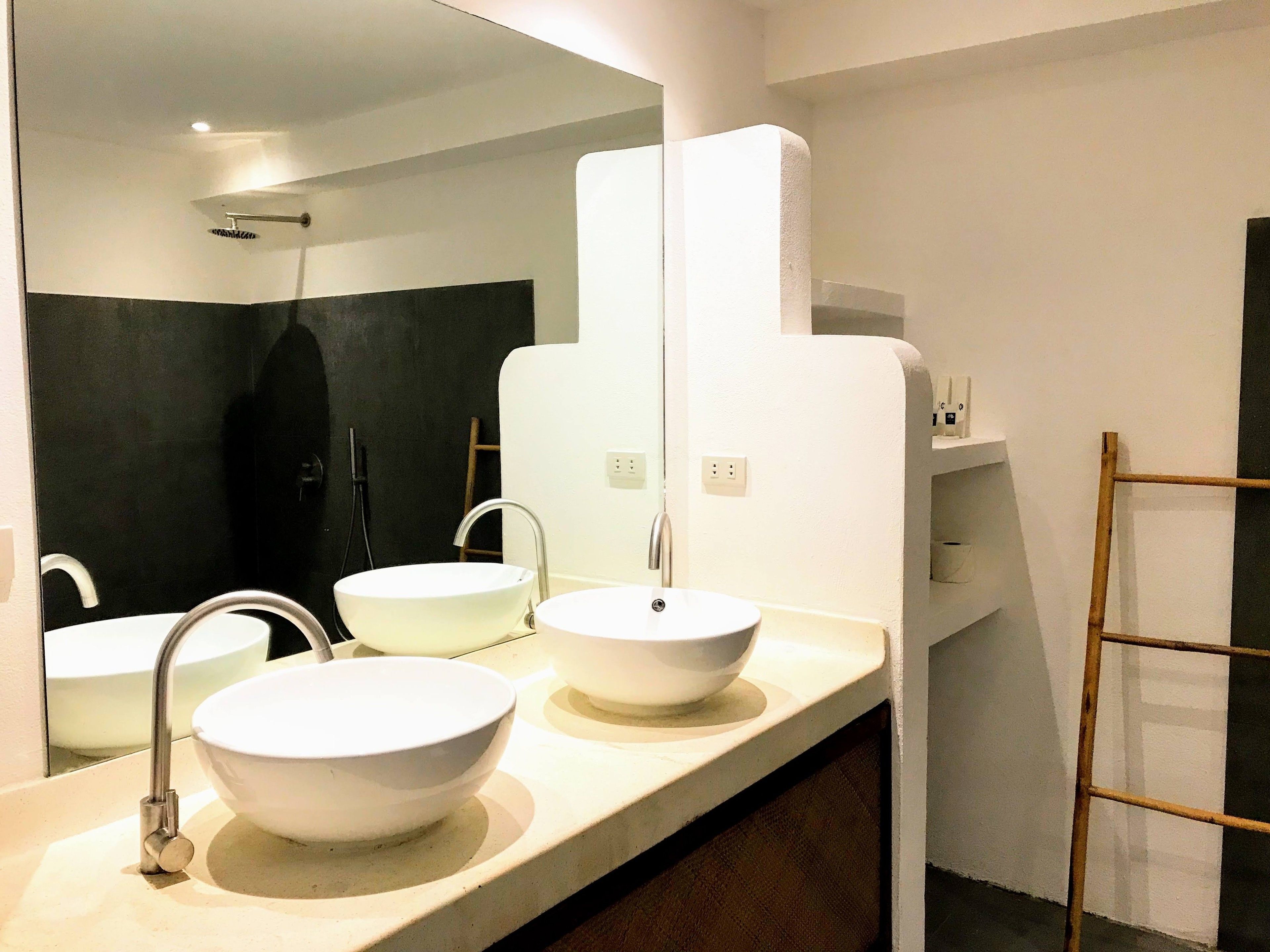 Casa de banho moderna com três lavatórios brancos, um espelho grande e área de chuveiro.