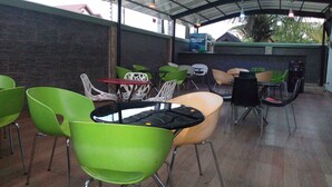 An outdoor cafe with green and white chairs, a black table, and a brick wall. - Dionzec Hotel & Suites (Lagos)