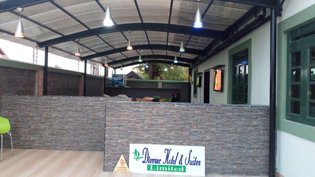 A covered outdoor area with a sign for Dioncec Hotel & Suites Limited, featuring a brick wall, hanging lights, and a wooden floor. - Dionzec Hotel & Suites (Lagos)