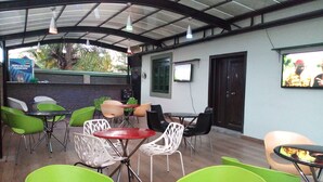 An outdoor seating area with green and white chairs, a red table, and a TV screen mounted on the wall. - Dionzec Hotel & Suites (Lagos)