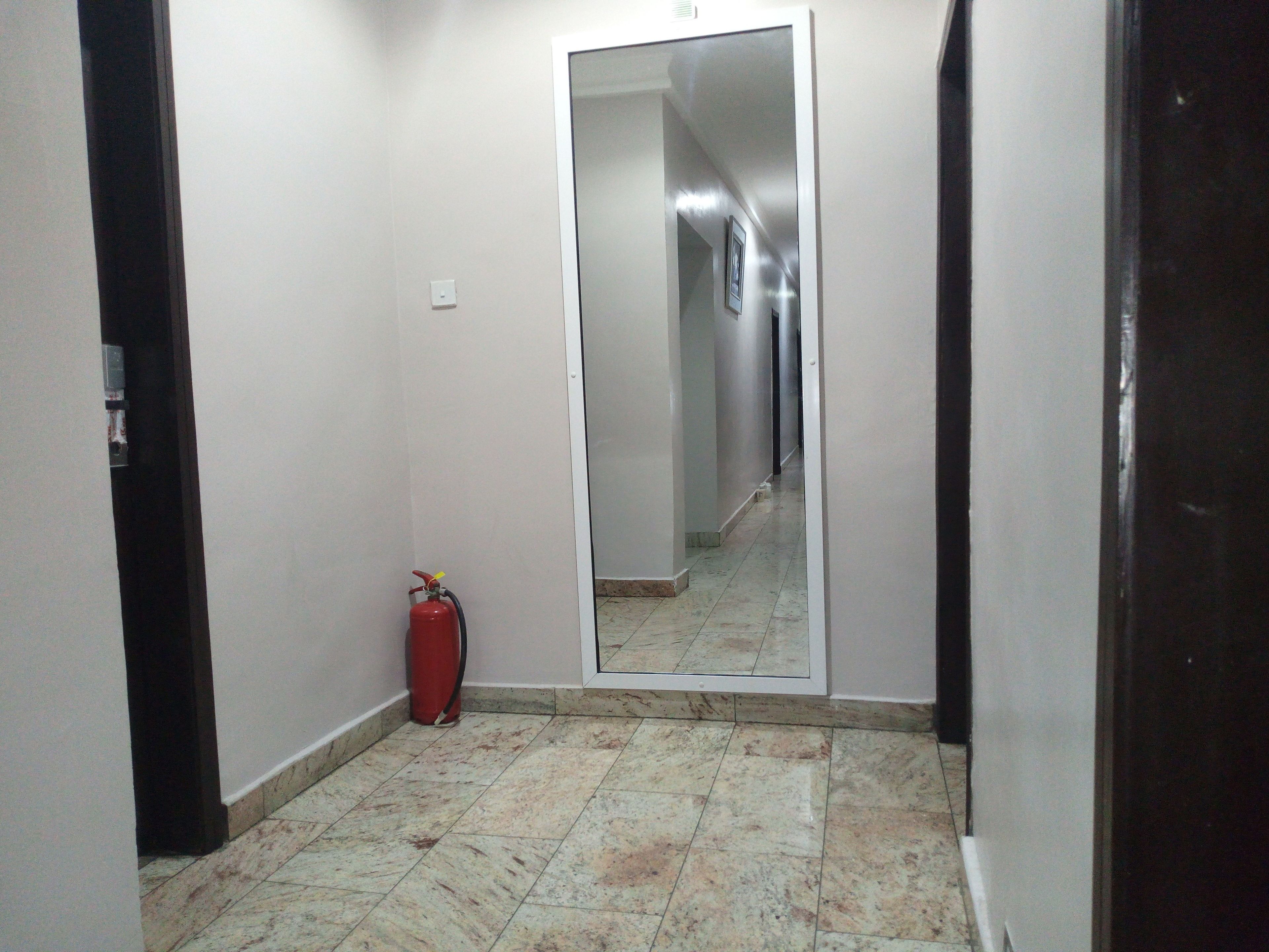 A narrow hallway with a fire extinguisher and a red suitcase on the floor.