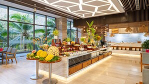 A modern hotel lobby with a large breakfast buffet, large windows with a view of palm trees, and a geometric ceiling design. - Rosa Alba Resort & Villas Tuy Hoa (Tuy Hoa)