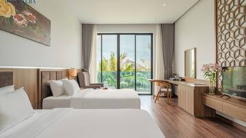 A hotel room with two beds, a desk, a TV, and a balcony with a view of palm trees.