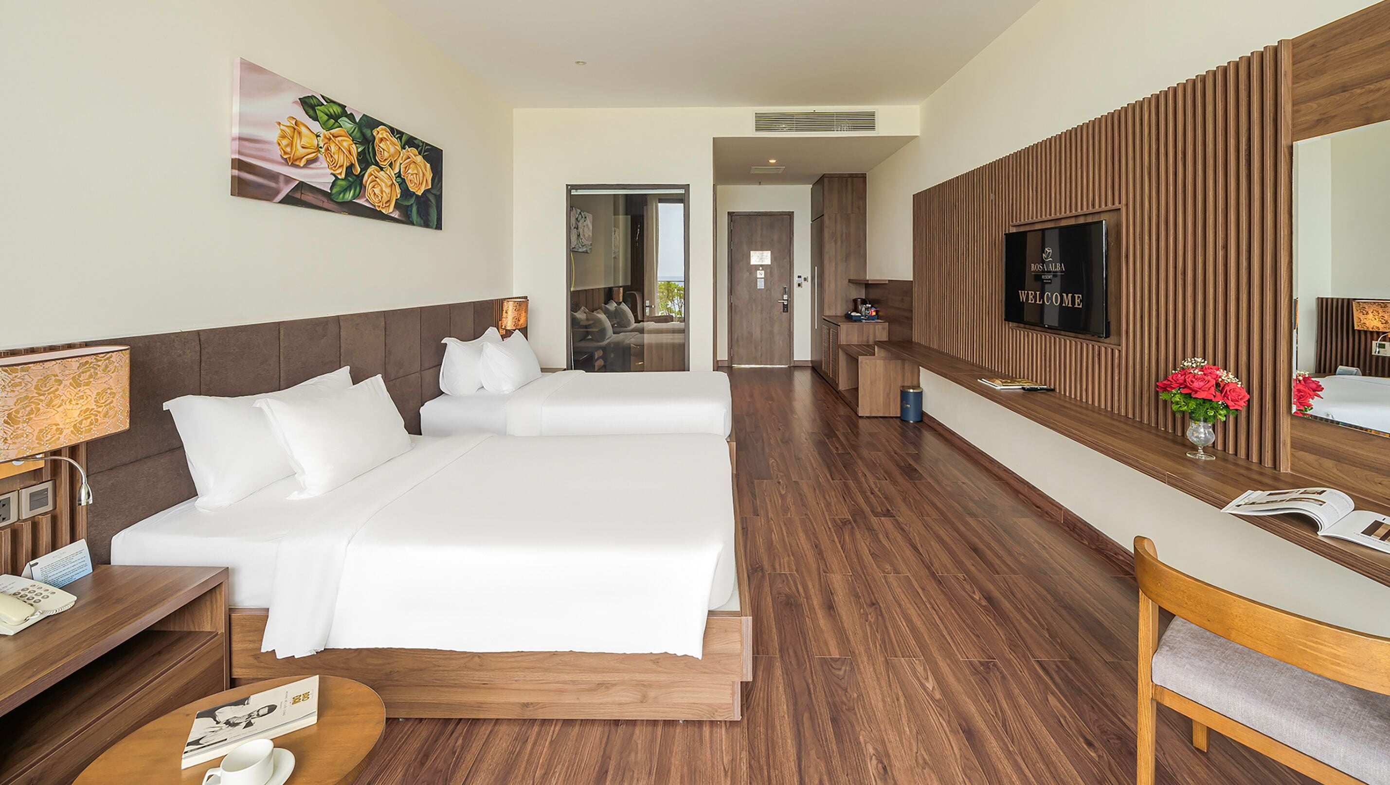 A hotel room with a large bed, a desk with a lamp, a TV, and a painting of flowers.