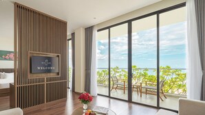 A modern hotel room with a large balcony, a television, a round wooden table with fruit and flowers, and a sofa. - Rosa Alba Resort & Villas Tuy Hoa (Tuy Hoa)