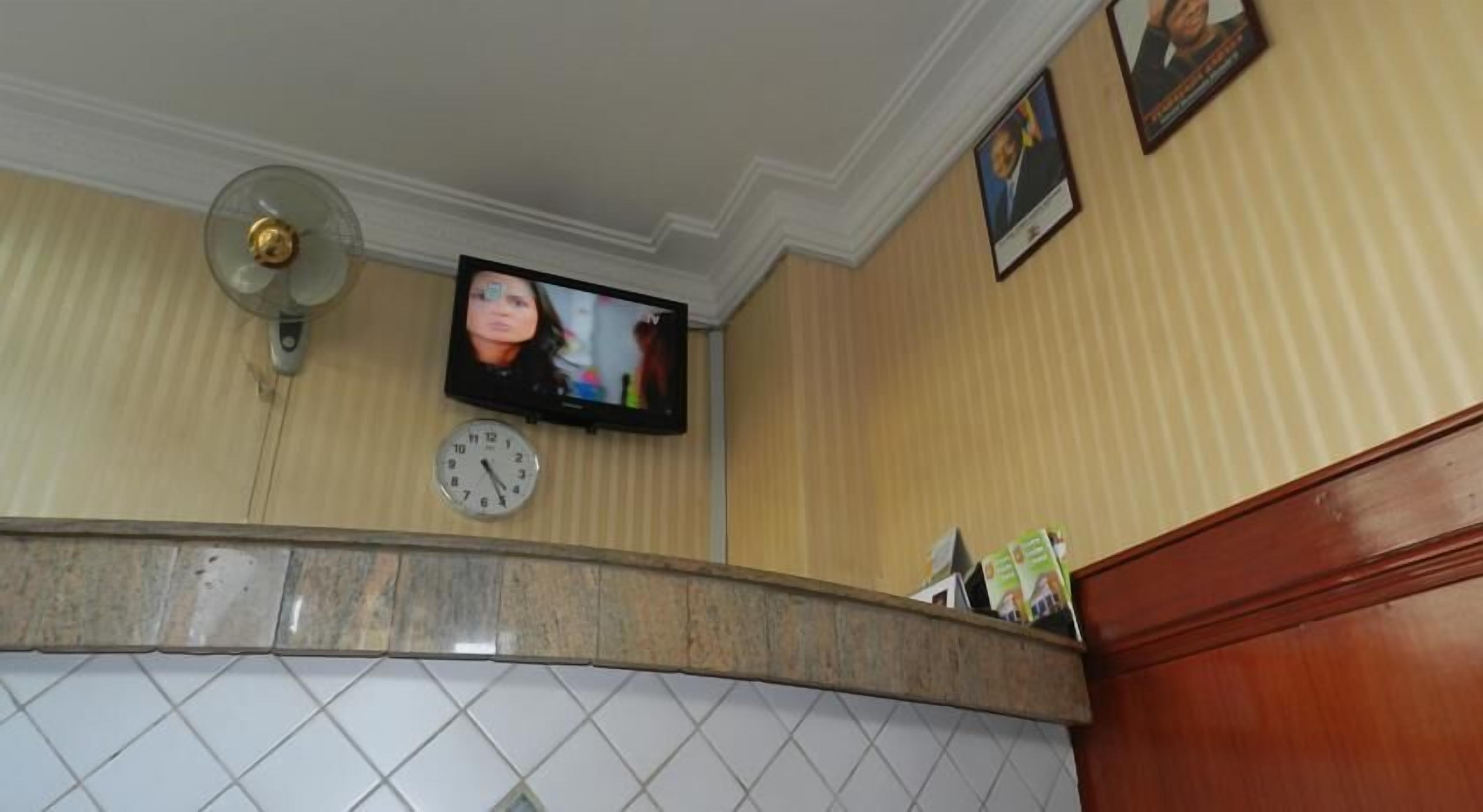 A bathroom with a clock, a television mounted on the wall, and a fan.