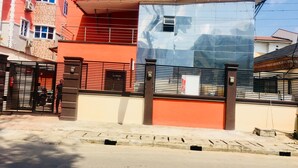 A modern building with a red facade, a large glass window, and a black metal gate. - Esporta Hotel Yaba (Lagos)
