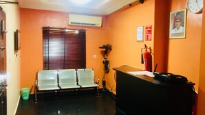 A reception area with a desk, chairs, a fire extinguisher, and a clock on the wall. - Esporta Hotel Yaba (Lagos)