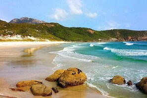 A beach with clear turquoise waters, large rocks, and green hills in the background. - Prom Coast Apartments (Sandy Point)