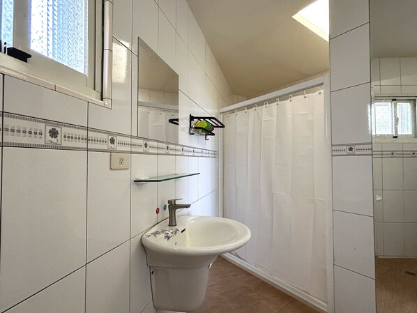 Un baño con azulejos blancos, un lavabo, un espejo y una cortina de ducha.