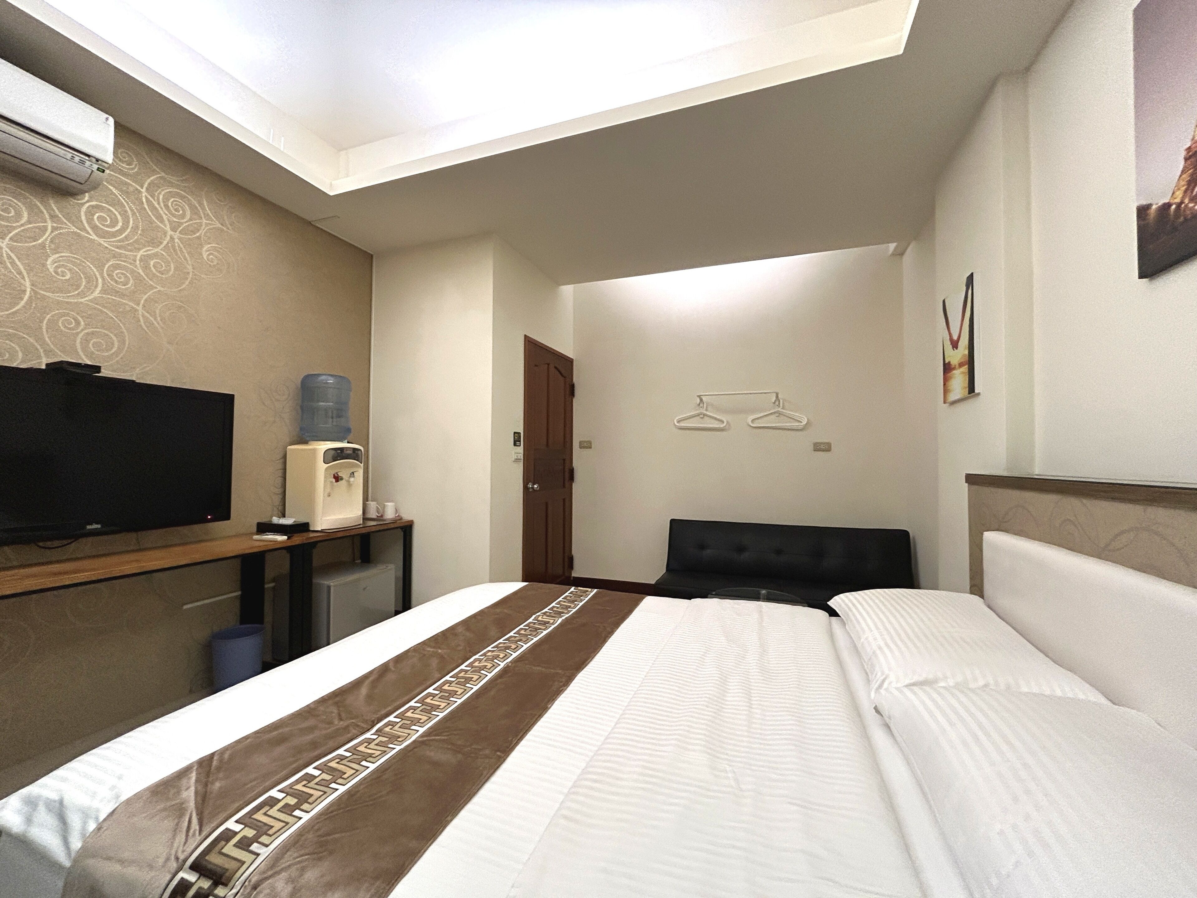 Une chambre d’hôtel équipée d’un lit, d’une télévision, d’un distributeur d’eau et d’une porte donnant sur une autre pièce.