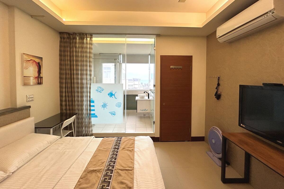 A hotel room with a bed, a desk, a television, and a sliding door leading to a bathroom.