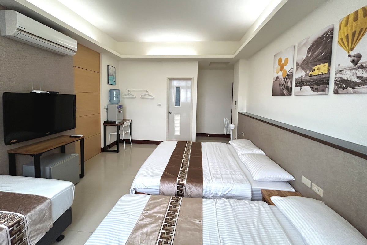 A hotel room with two beds, a television, a water dispenser, and a desk.