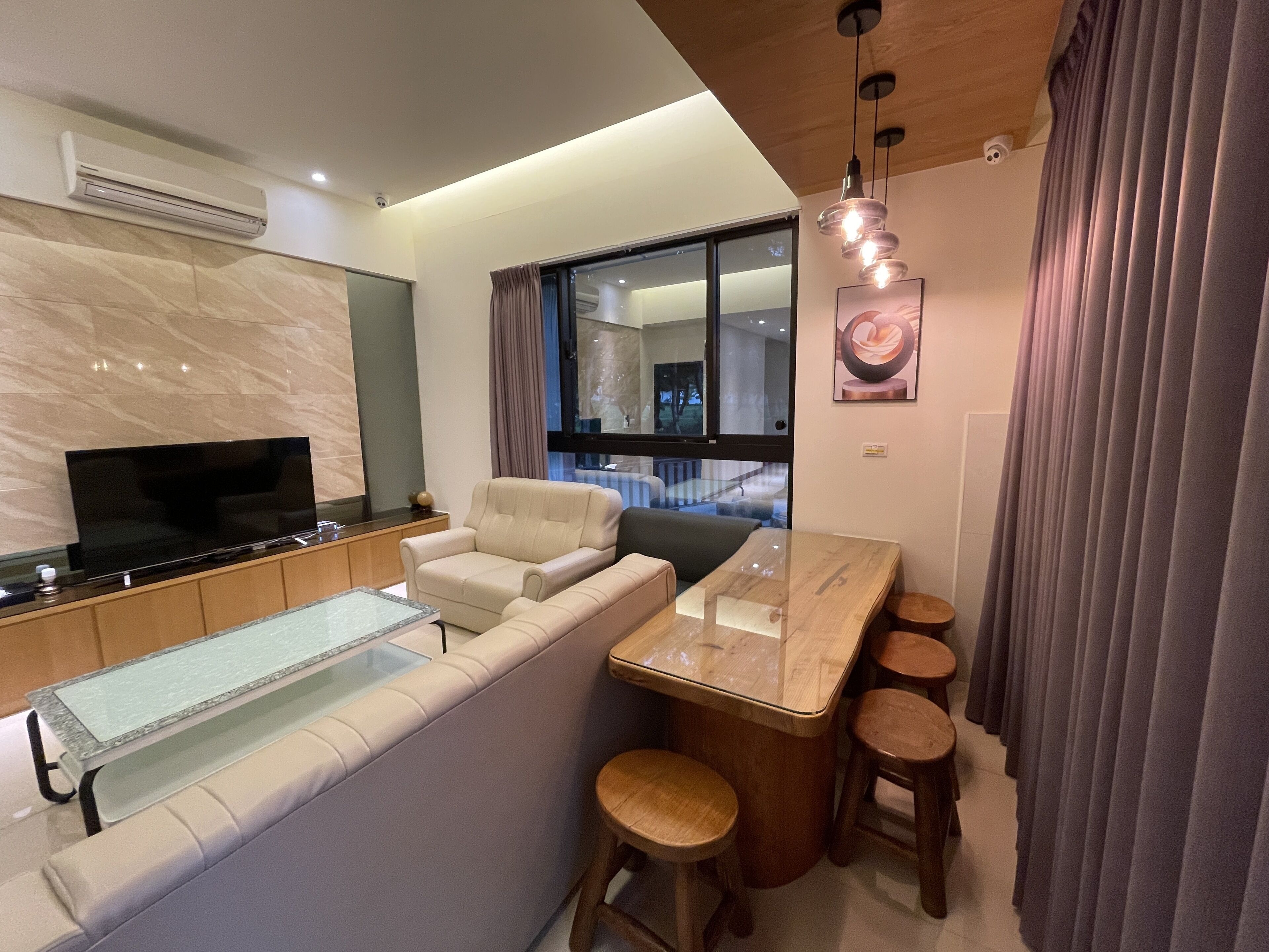 A modern living room with a sofa, a TV, a glass-top coffee table, and a bar area with stools.
