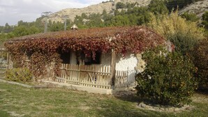Un bâtiment rustique aux murs couverts de lierre, avec une clôture en bois et une chaîne de montagnes en arrière-plan.