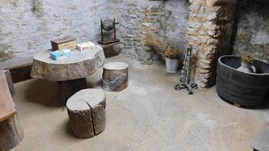 Un intérieur rustique avec des murs en pierre, une table en bois surmontée de boîtes, un pot en métal et un tonneau.