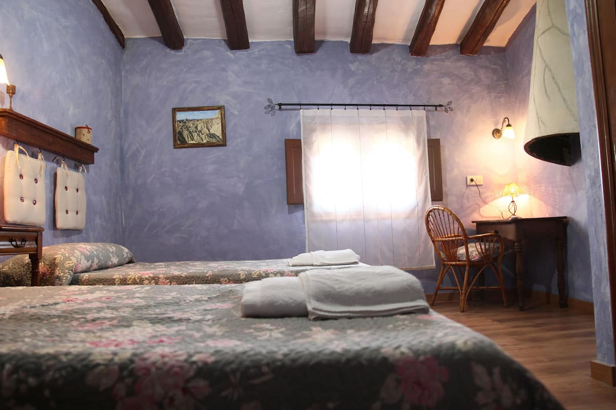 A bedroom with two beds, a desk, a chair, and a window with curtains.