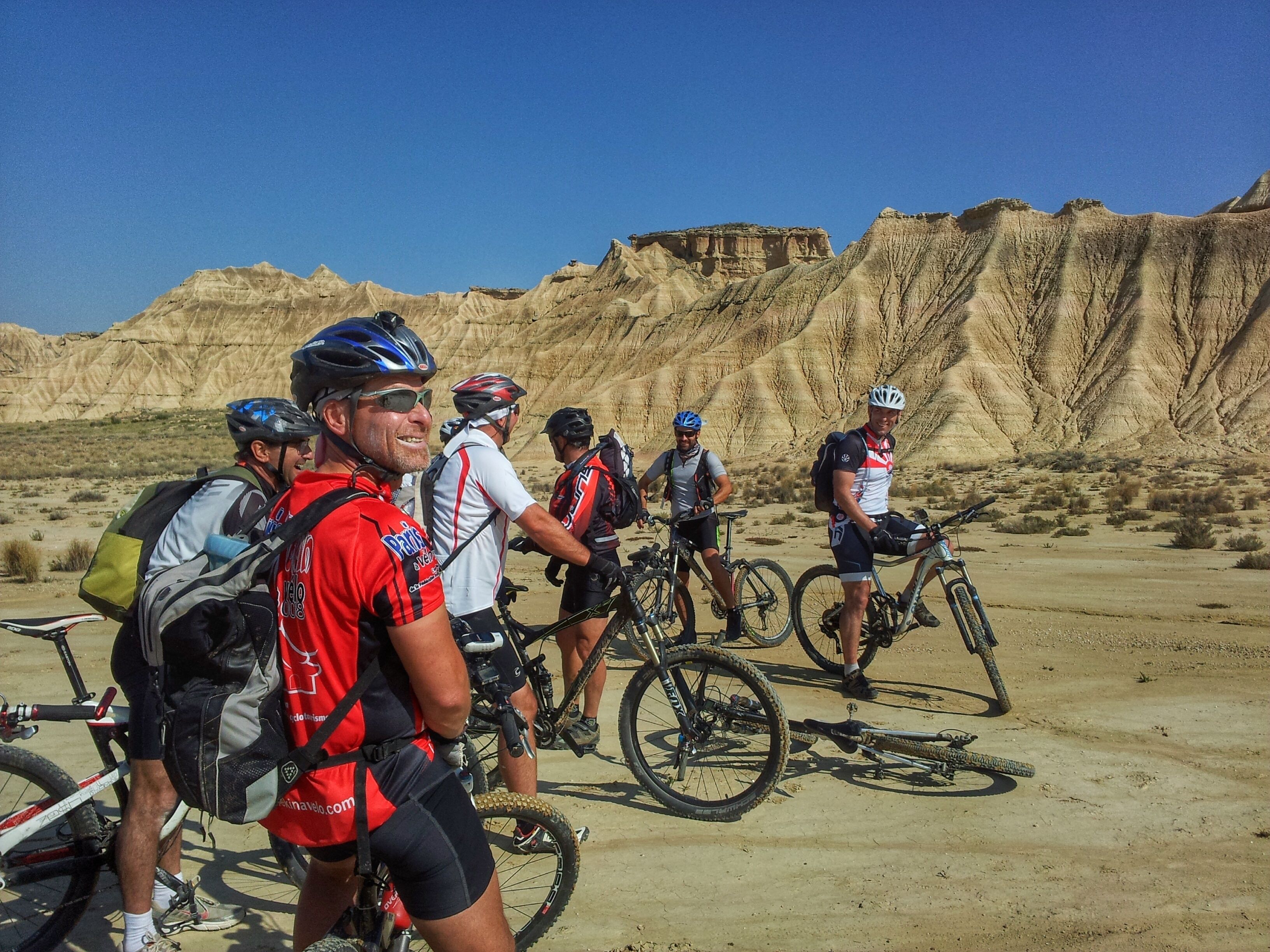 A group of cyclists in a desert landscape with rocky terrain and sparse vegetation.