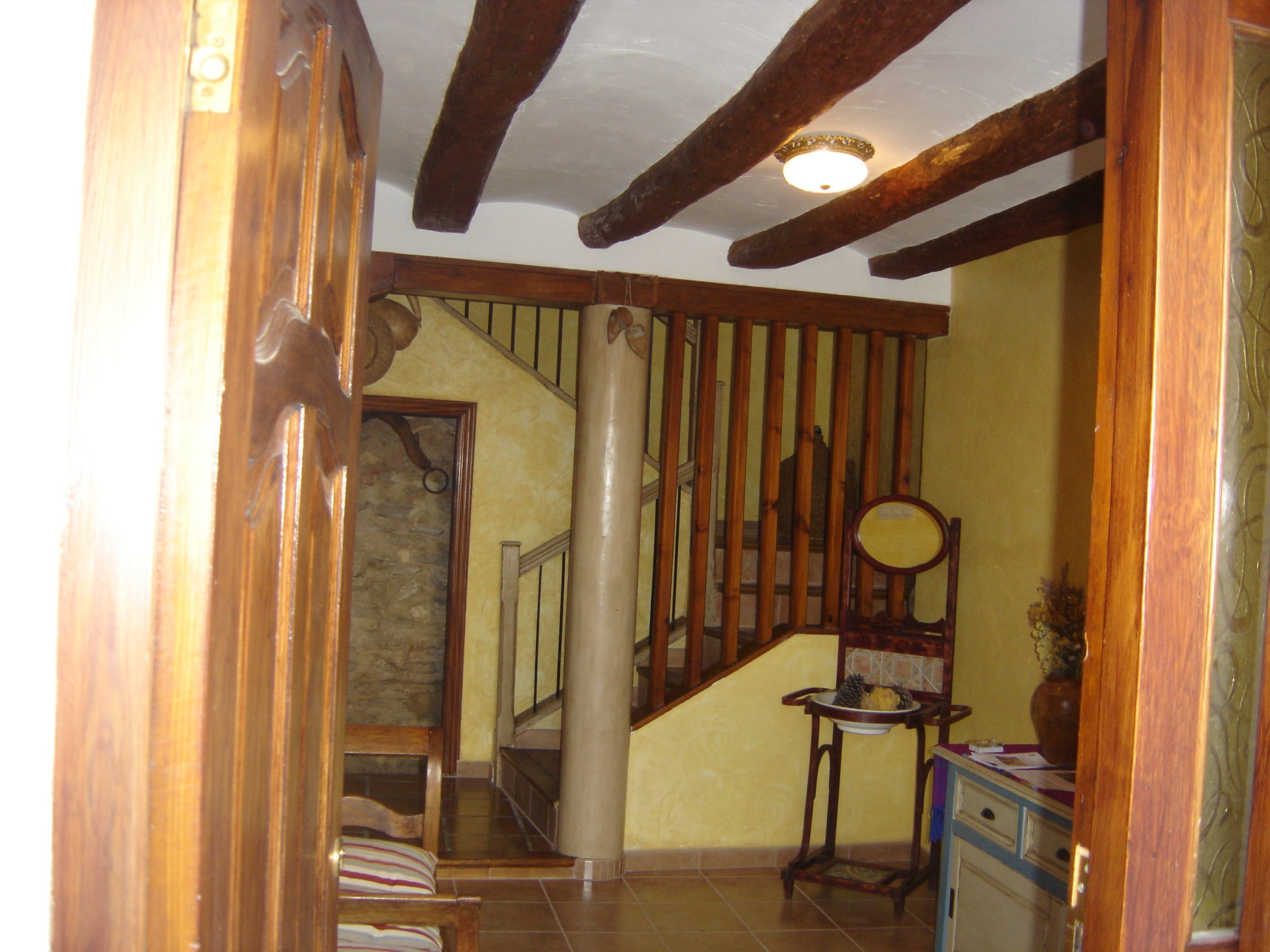 Un escalier avec des balustrades en bois, une chaise en bois, une petite table avec un bol et des pommes de pin, et un miroir accroché au mur.