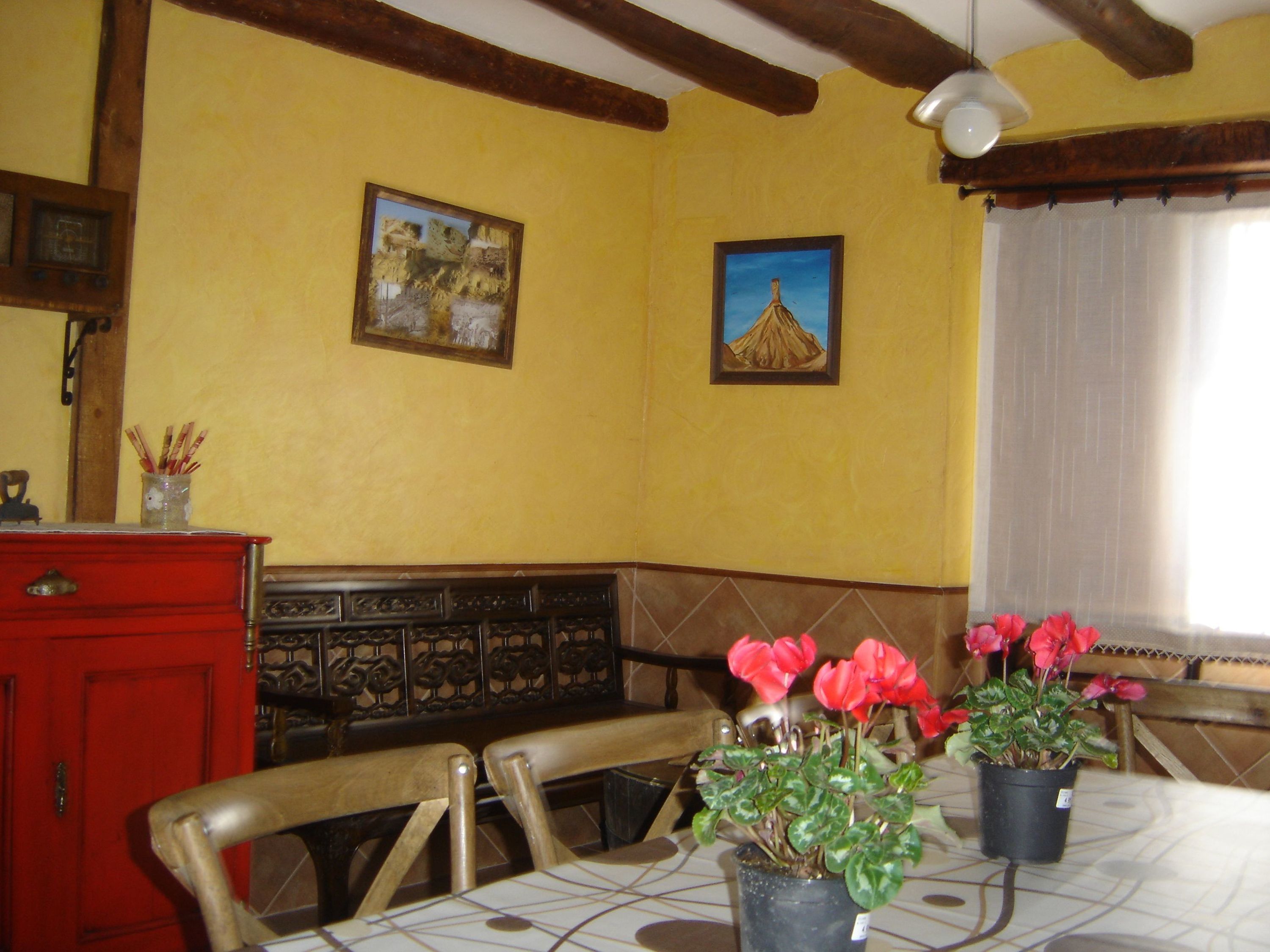 Un comedor con una mesa, sillas, un armario rojo y dos macetas con flores.