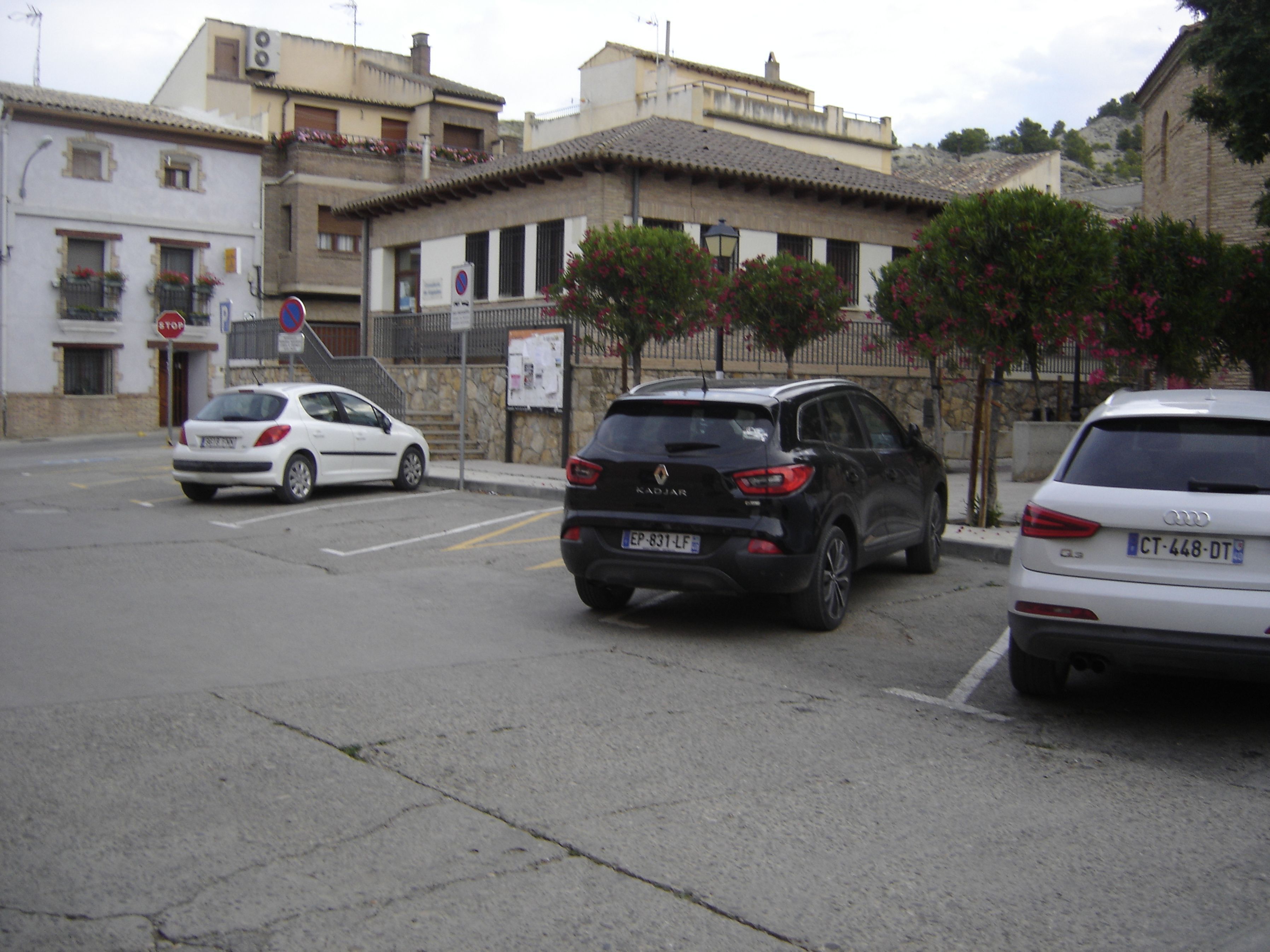 A street with parked cars, a building with a stone facade, and a signboard.