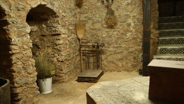 Une pièce aux murs de pierre, avec une table en bois, un balai et une plante en pot.