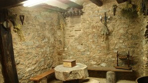 Une pièce rustique aux murs de pierre, avec un banc en bois, une table ronde et un tonneau.