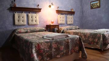 Ein Schlafzimmer mit zwei Betten, jeweils mit floralem Bettzeug und passenden Kissen. An der Wand sind Leuchten befestigt und es steht ein kleiner Tisch mit einer Lampe bereit.