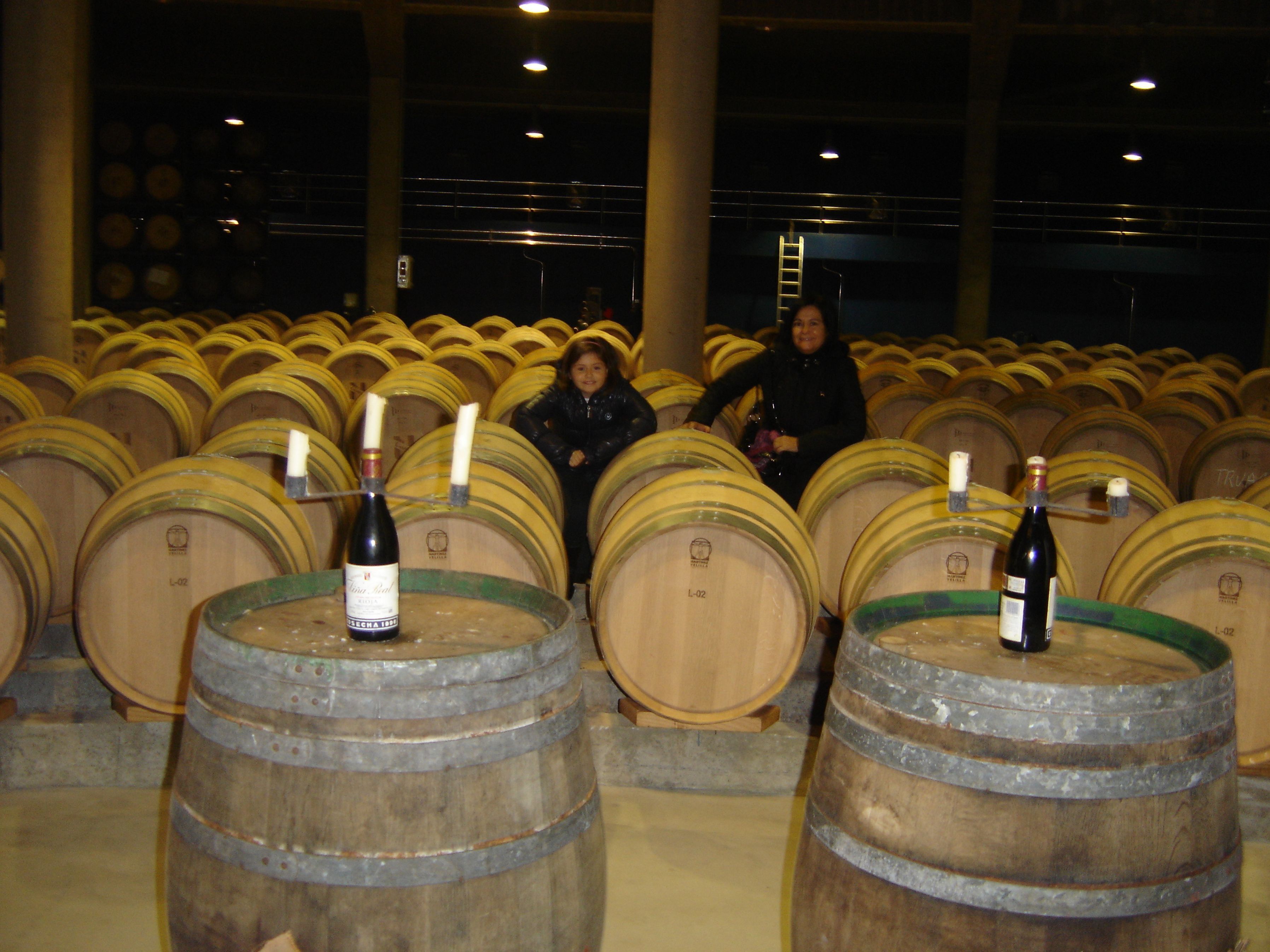 Una bodega con hileras de barriles de madera, algunos con botellas encima.