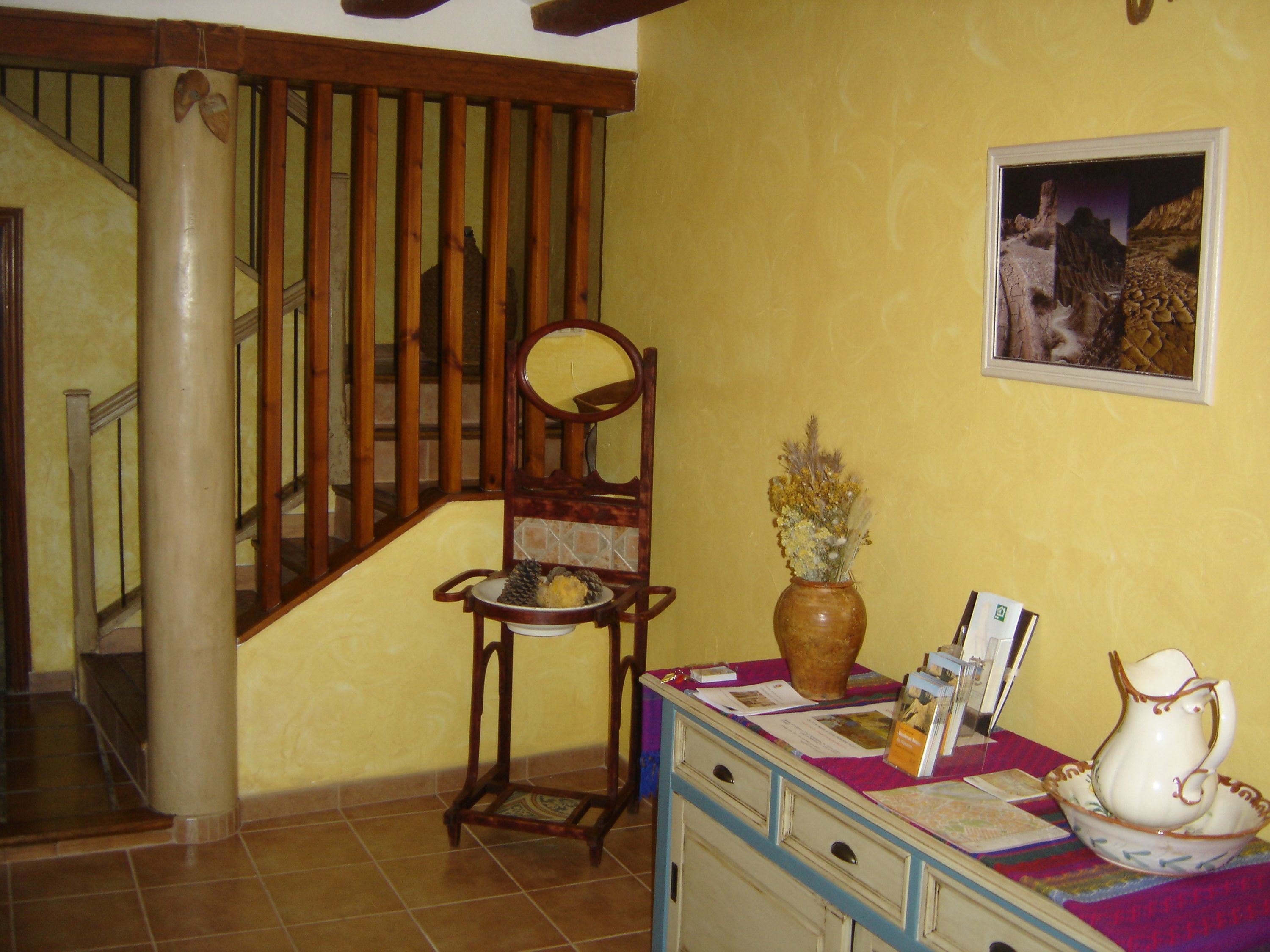 A staircase with wooden railings, a chair with a vase of dried flowers, and a table with a pitcher and brochures.
