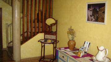 A staircase with wooden railings, a chair with a vase of dried flowers, and a table with a pitcher and brochures.