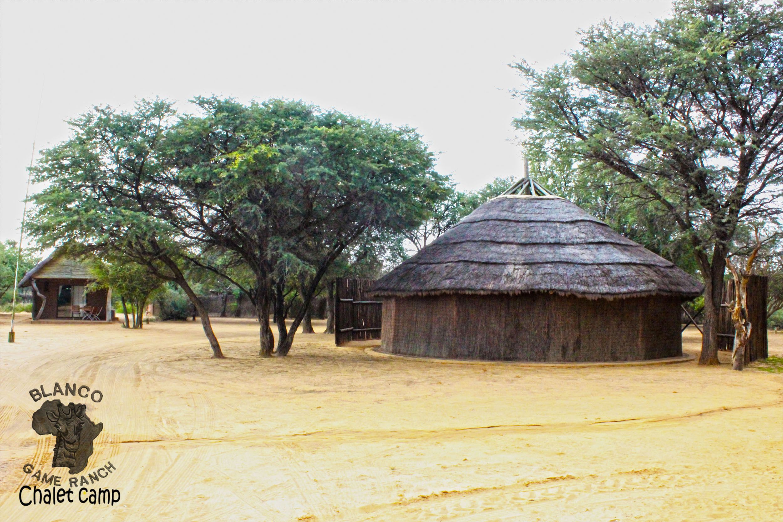 A thatched-roof structure in a rural setting with a dirt road leading to it.