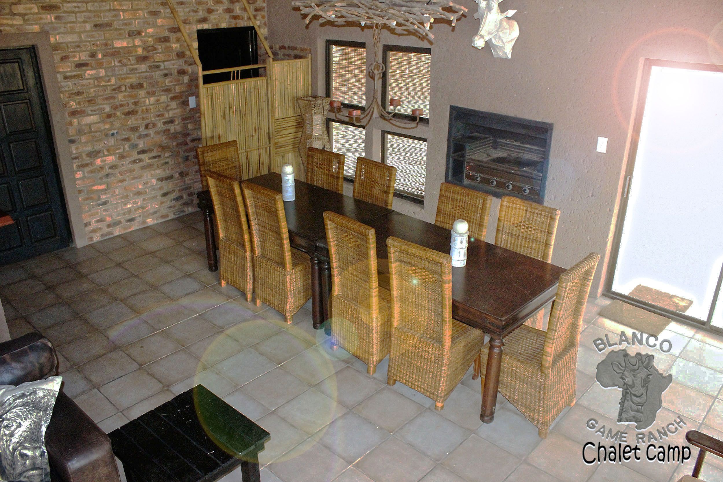 Un espace repas avec une longue table en bois et des chaises en osier, un mur en briques et une cheminée.