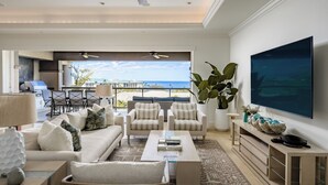 Een moderne woonkamer met een bank, fauteuils, een salontafel en een televisie. Er is een balkon met uitzicht op de oceaan.