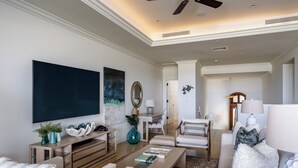 Een moderne woonkamer met een flatscreen televisie, comfortabele zithoek, een salontafel en een eethoek met een lamp.